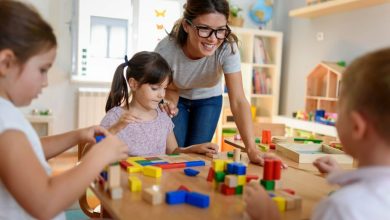 Preschool teacher with children playing with colorful wooden didactic toys at kindergarten